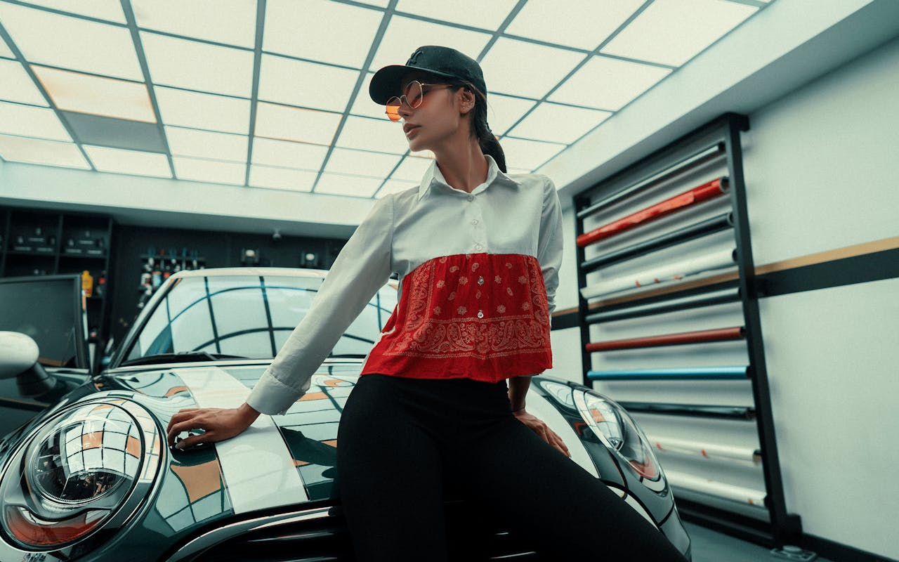 Fashionable woman posing by a car in a modern garage setting with vibrant lighting.