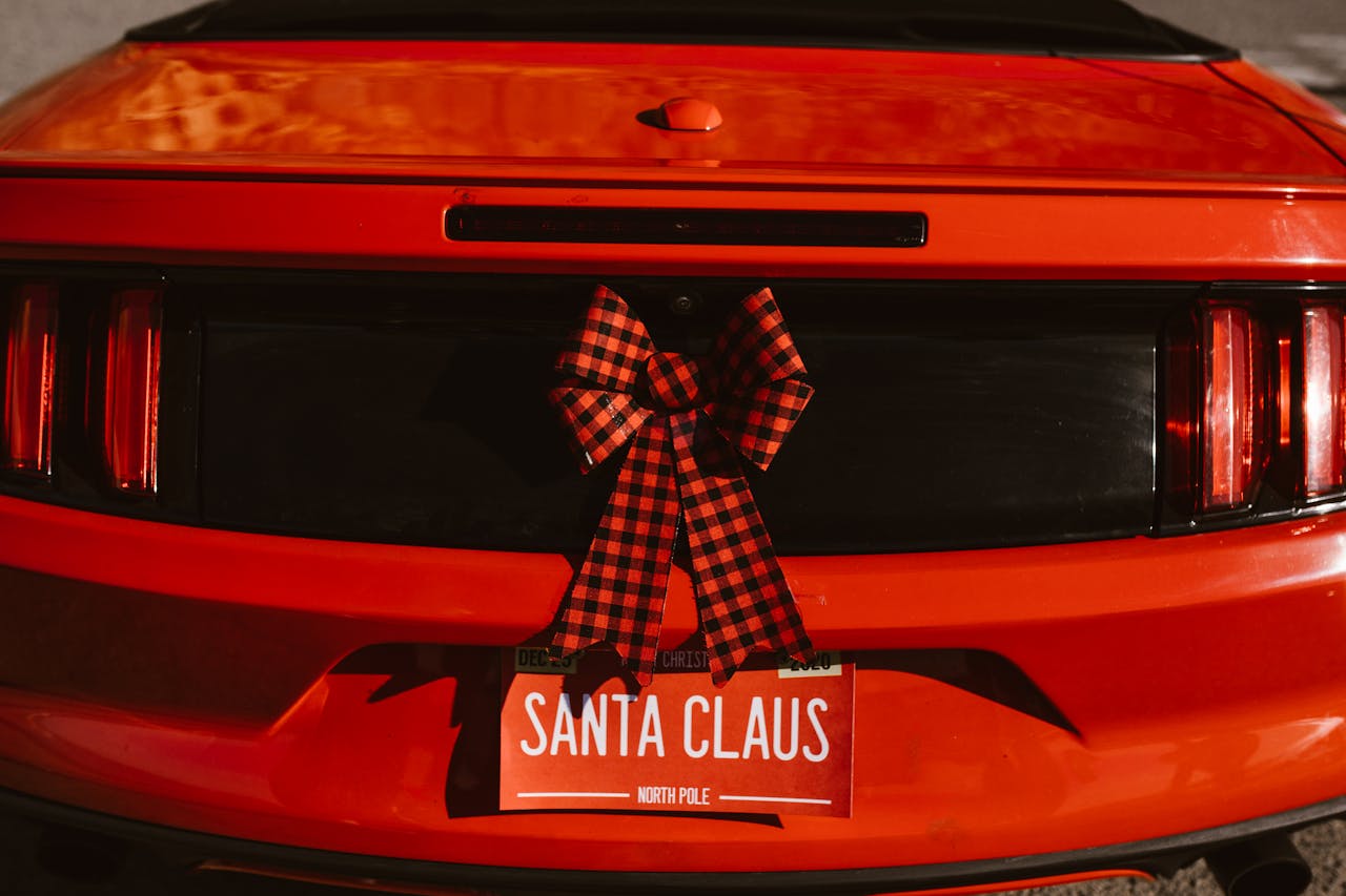 Red car with Santa Claus-themed license plate and holiday bow decoration.